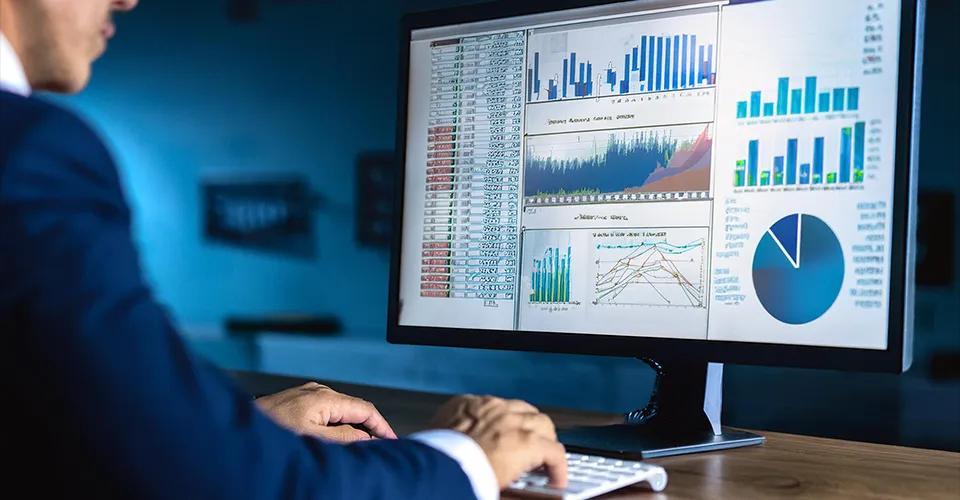 Eine Person in einem Anzug sitzt vor einem Computerbildschirm, der verschiedene Finanzdiagramme, Balkendiagramme und Tabellen zeigt. Die Diagramme scheinen Geschäftsdaten und Quartalsberichte darzustellen. Die Person arbeitet in einem modernen, blau beleuchteten Büro, wobei der Fokus auf den Daten und Analysen auf dem Bildschirm liegt.